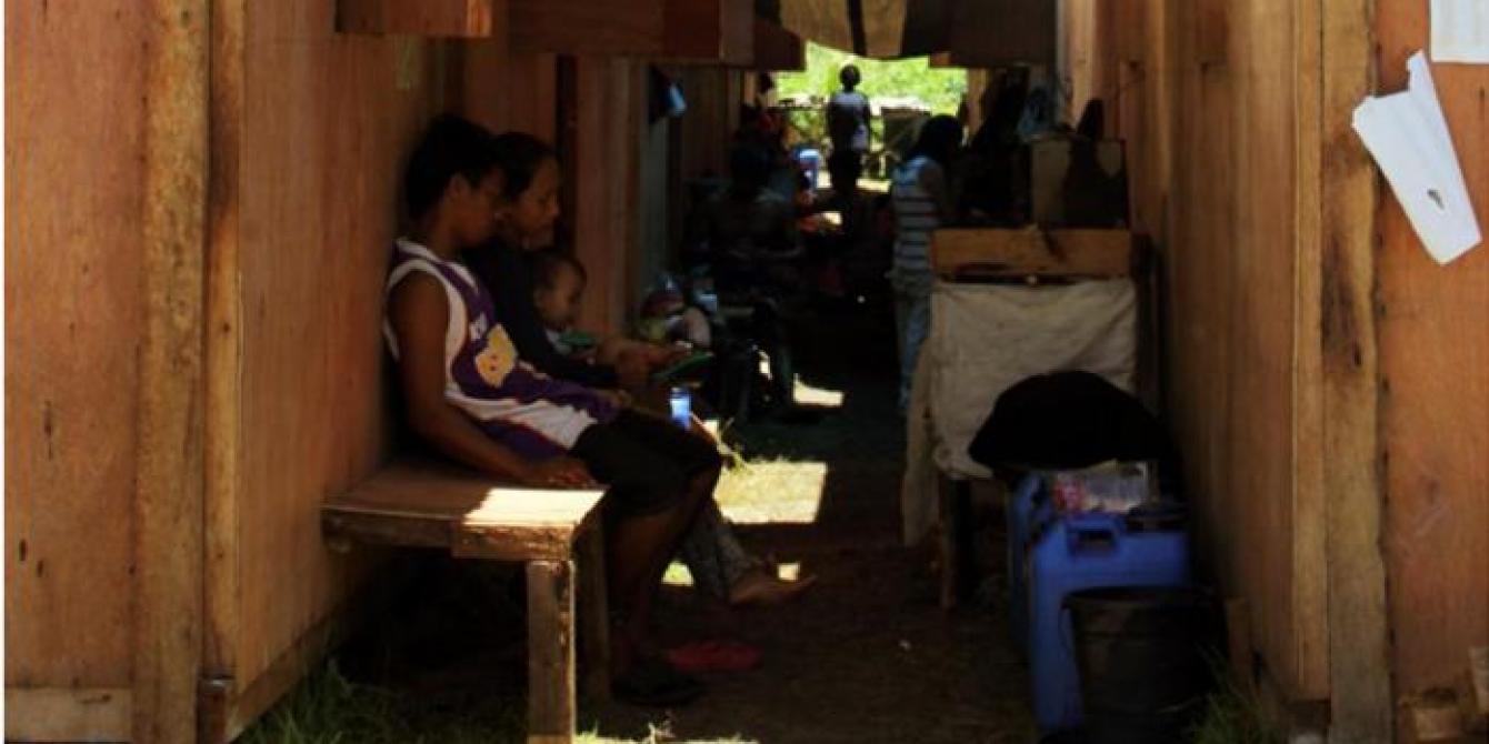 A family sits outside the bunkhouse where they continue to live after being displaced by typhoon Haiyan. Many of those in bunkhouses are being targeted for permanent resettlement to safer land as part of recovery plans. Photo: Genevive Estacaan/Oxfam 2014 A family sits outside the bunkhouse where they continue to live after being displaced by typhoon Haiyan. Many of those in bunkhouses are being targeted for permanent resettlement to safer land as part of recovery plans. Photo: Genevive Estacaan/Oxfam 2014